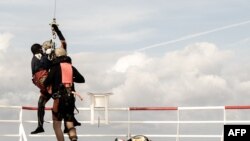 A migrant in need of urgent medical care (L) is about to be winched up from the Ocean Viking rescue ship by a French Army helicopter, in the Tyrrhenian Sea between Italy and Corsica island.