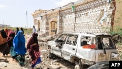 FILE - Women walk next to a destroyed house and the wreckage of a car following an explosion provoked by Al-Shabaab militants' during an attack to a police station on the outskirts of Mogadishu, Somalia, on February 16, 2022.