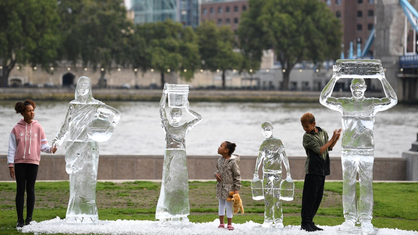 Children pose by ice sculptures depicting people collecting water by charity Water Aid to show the fragility of water and the threat posed by climate change on September 15, 2021 in London. 