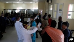 FILE - Afghan health workers measure the temperature of Afghan refugees to screen for coronavirus as they enter Afghanistan at the Islam Qala border crossing with Iran, in the western Herat Province, March 18, 2020.