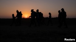 FILE - The sun rises as asylum-seeking migrant families from Honduras and El Salvador walk toward the border wall after crossing the Rio Grande into the United States from Mexico on a raft in Penitas, Texas, on March 26, 2021. 