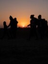 FILE - The sun rises as asylum-seeking migrant families from Honduras and El Salvador walk toward the border wall after crossing the Rio Grande into the United States from Mexico on a raft in Penitas, Texas, on March 26, 2021. 