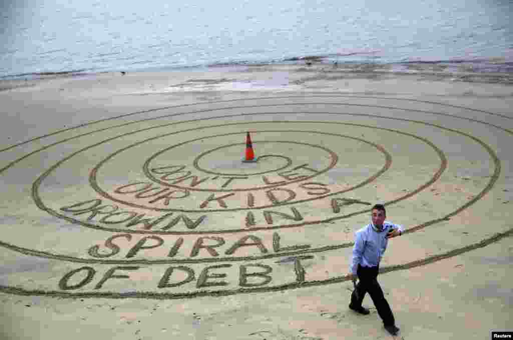 یک مرد معترض به افزایش بدهی های بریتانیا، در یک مارپیچی که روی خاک ساحل رودخانه تمز کشیده، نوشته اجازه ندهید فرزندان ما هم در مارپیچ بدهی ها غرق شوند.