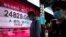 People wearing face masks walk past a bank's electronic board showing the Hong Kong share index in Hong Kong, July 29, 2020. 