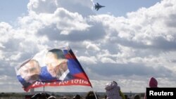 A spectator waves a flag depicting images of Russian President Vladimir Putin (L) and Prime Minister Dmitry Medvedev as a Sukhoi SU-34 fighter-bomber performs during the MAKS International Aviation and Space Salon in Zhukovsky outside Moscow, Russia, Aug. 30, 2015.