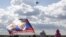 A spectator waves a flag depicting images of Russian President Vladimir Putin (L) and Prime Minister Dmitry Medvedev as a Sukhoi SU-34 fighter-bomber performs during the MAKS International Aviation and Space Salon in Zhukovsky outside Moscow, Russia, Aug. 30, 2015.