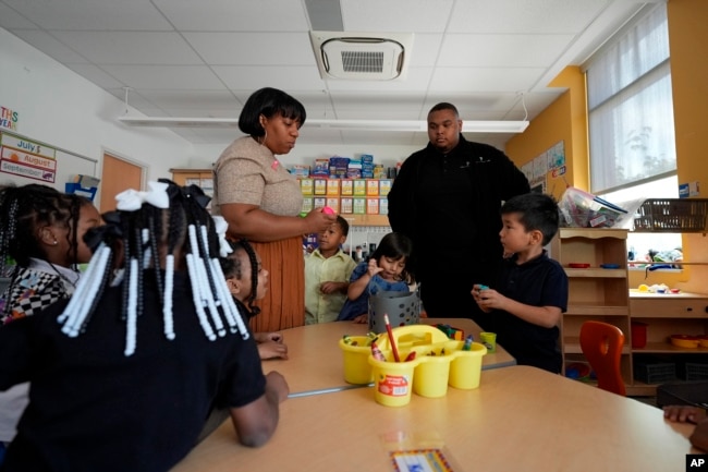 Preschool teacher Bridget Jeffreys and Leading Men fellow Davontez Johnson are surrounded by students, Oct. 3, 2024, at Dorothy I. Height Elementary School in Baltimore. (AP Photo/Stephanie Scarbrough)