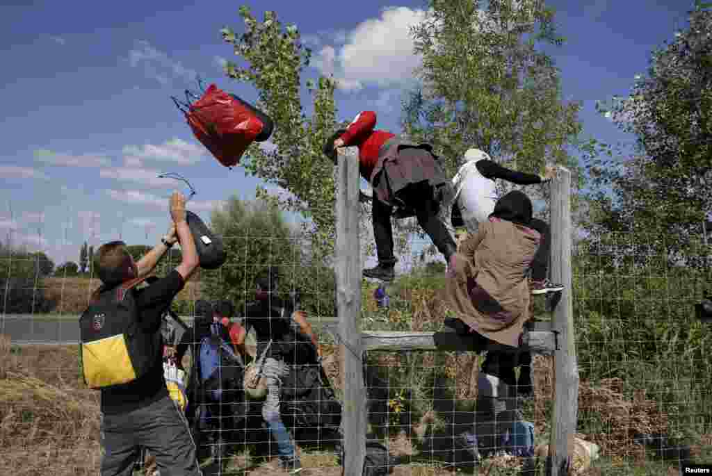 Migrants jump over a road protection fence as they leave a collection point in the village of Roszke.