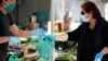 Un vendeur portant un masque protecteur livre un sac en plastique à un client d'un marché alimentaire en plein air qui a rouvert après le confinement dû au coronavirus à Cisternino, en Italie, le 27 avril 2020. REUTERS / Alessandro Garofalo - RC20DG9J93DO