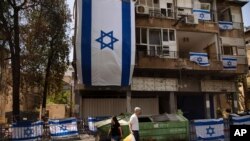 People walk by a residential building covers with Israeli flags after last week it was hit by a rocket fired from the Gaza Strip, in Ramat Gan, central Israel, May 21, 2021.