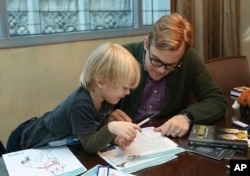 Adam Bryan and his son Wesley work together on puzzles included in complimentary backpacks provided with other incentives by the Wyndham Grand Hotel in Chicago on Dec. 1, 2018. (AP Photo/Teresa Crawford)