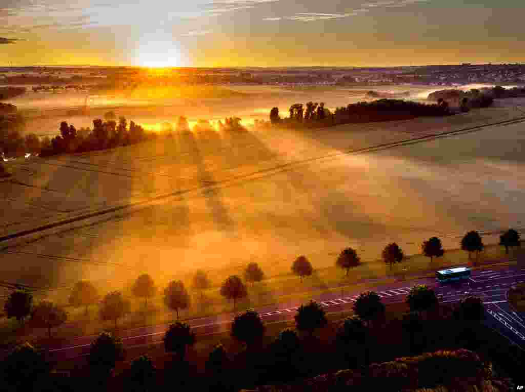 A bus is driven through an alley as the sun rises over fog covered field on the outskirts of Frankfurt, Germany.