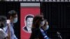 Warga China yang mengenakan masker melewati foto Presiden Xi Jinping di Shanghai (foto: dok). China merilis laporan panjang dan mengklaim kemenangan atas Covid-19 hari Senin (8/6). 