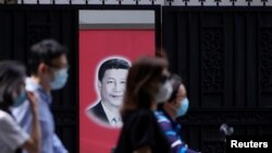 Warga China yang mengenakan masker melewati foto Presiden Xi Jinping di Shanghai (foto: dok). China merilis laporan panjang dan mengklaim kemenangan atas Covid-19 hari Senin (8/6). 