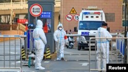 Workers in protective suits stand at an entrance to a university's residential area under lockdown following the coronavirus disease (COVID-19) outbreak in Xian, Shaanxi province, China, Dec. 20, 2021. (China Daily via Reuters)