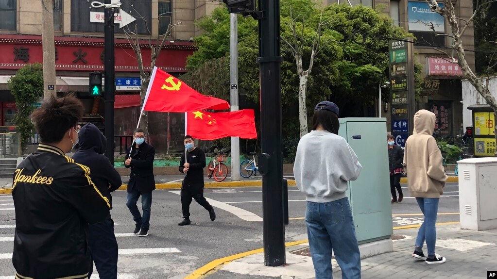 上海静安区居民排队做新冠病毒核酸检测，路上有人打着中共与中国的旗帜走过。（2022年4月1日）(photo:VOA)