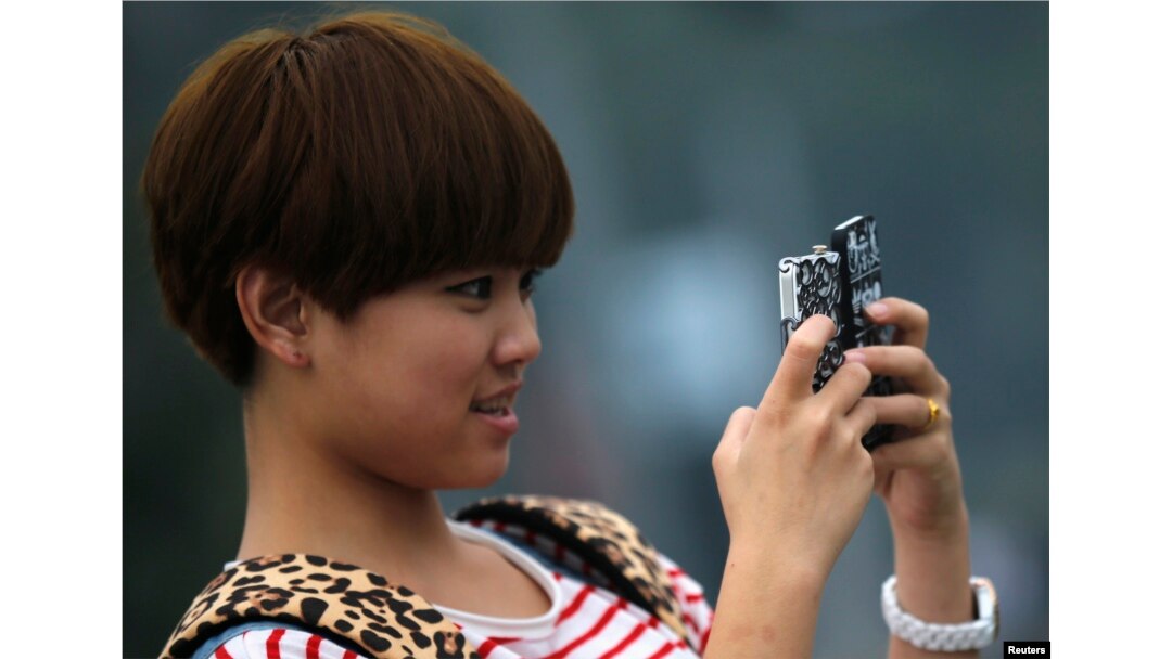 Seorang remaja perempuan memegang dua ponsel saat berfoto di pusat kota Shanghai, 22 Oktober 2012.