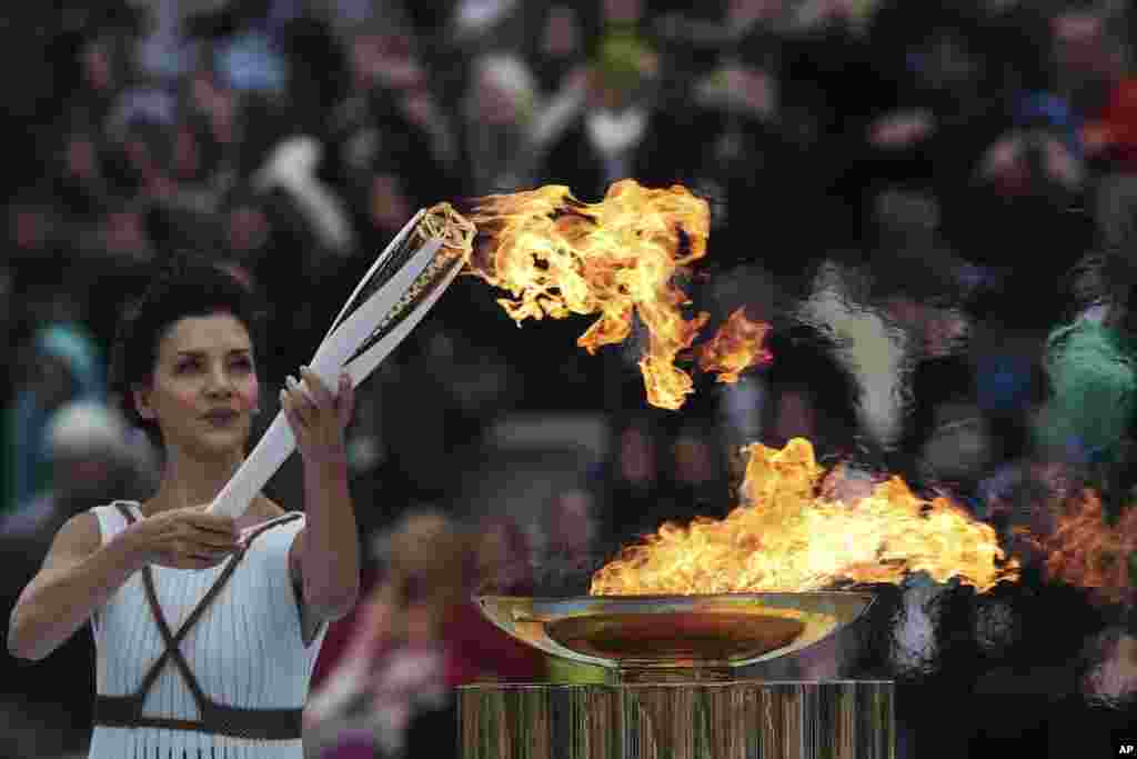 Actress Katerina Lehou, playing the role of high priestess, lights an Olympic torch during a handover ceremony for the Olympic Flame at Panathenaic stadium in Athens, Greece.