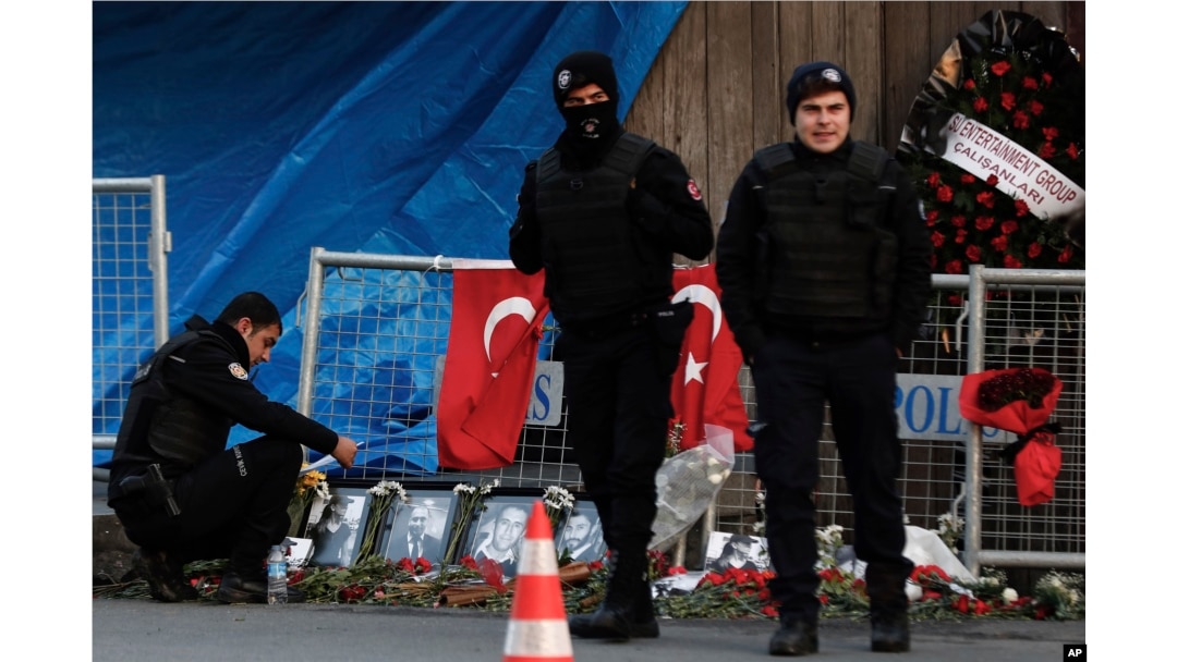 Un oficial de policía observa las fotografías de las víctimas mientras otros dos vigilan un día después del ataque al popular club nocturno en Estambul.