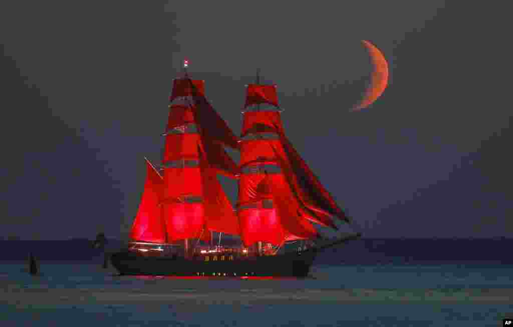 A brig with scarlet sails travels on the Finnish Gulf coast during a rehearsal for the Scarlet Sails festivities marking school graduation which will take place on June 27 in St. Petersburg, Russia, with the setting moon in the background. 