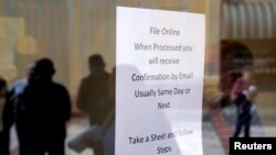 FILE - People who lost their jobs are reflected in the door of an Arkansas Workforce Center as they wait in line to file for unemployment following an outbreak of the coronavirus disease (COVID-19), in Fort Smith, Arkansas.