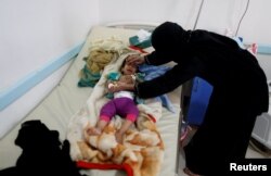 FILE - A woman helps her son as he lies on a bed at a cholera treatment center in Sanaa, Yemen, June 6, 2017.