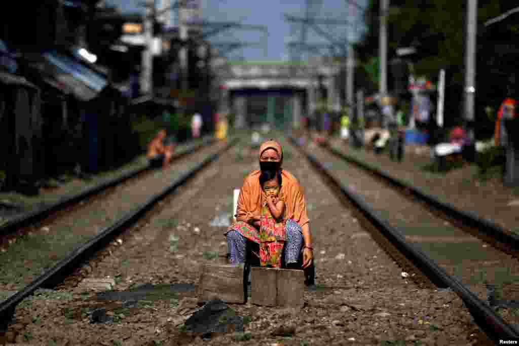 A woman wearing a face mask and a child sit on rail tracks in Jakarta, Indonesia.