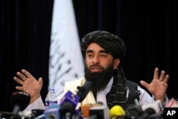 In front of a Taliban flag, Taliban spokesman Zabihullah Mujahid speaks at at his first news conference, in Kabul, Afghanistan, Tuesday, Aug. 17, 2021. (AP Photo/Rahmat Gul)