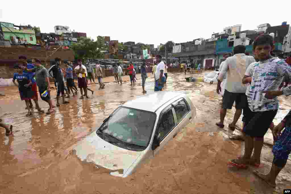 People stand next to a car partially covered in mud due to flooding after a heavy monsoon rainfall in Jaipur, India.