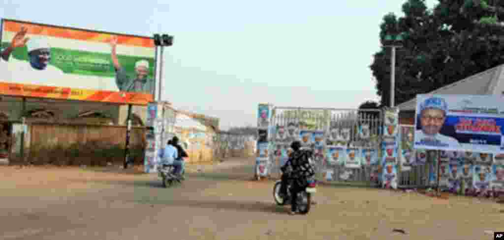 Members of the Party Loyalists drive their motocycles outside the entrance of a park in front of posters featuring Nigeria's opposition leader Mohammadu Buhari a (R) and Nigeria's President Goodluck Jonathan and his Vice President Namadi Sambo (L) in K