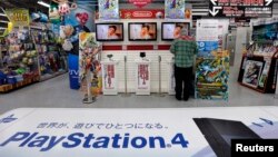 FILE - A man tries out Nintendo Co Ltd's 3DS portable game console near an advertisement for Sony's PlayStation 4 game console at an electronics retail store in Tokyo, May 7, 2014. 