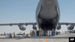 Evacuees wait under the wing of C-17 Globemaster lll after arriving in an undisclosed location in the Middle East region, Aug. 20, 2021, after being evacuated onboard a military aircraft from Hamid Karzai International Airport in Kabul, Afghanistan.