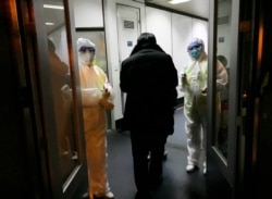 Health Officials in hazmat suits wait at the gate to check body temperatures of passengers arriving from the city of Wuhan, Jan. 22, 2020, at the airport in Beijing, China.