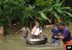 FILE - An elderly woman is rescued in a cooking pot after her home was flooded in Thrissur, Kerala state, India, Aug.16, 2018.