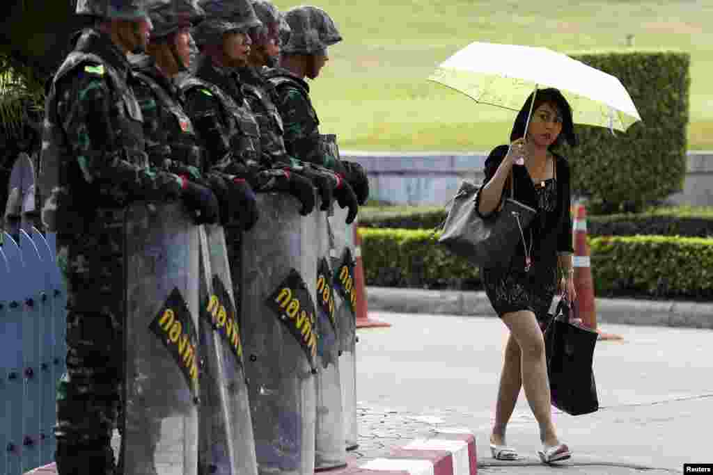 A woman walks past soldiers providing security to the Army Club where senior army officials are meeting foreign diplomats in Bangkok, May 23, 2014.