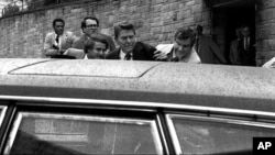 FILE - In this March 30, 1981, photo, U.S. president Ronald Reagan, center, is shown being shoved into his limousine by secret service agents after being shot outside a Washington hotel.