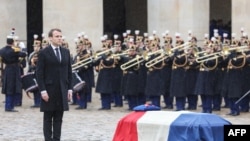 Prezidan fransè a, Emmanuel Macron (agoch) kanpe bò kote sèkèy Lyetnan-Kolonèl Arnaud Beltrame, aprè li te onore ofisye a, yon fason postim, avèk Meday Komandè "La Legion d'Honneur" nan yon antèman nasyonal ki dewoule nan kapital la, Pari, mèkredi 28 mas 2018 la nan lokal Hotel des Invalides. (Foto: AFP / Ludovic MARIN, 28 mas 2018).