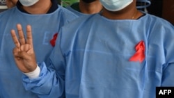 A medical staff makes a three finger salute with a red ribbon on a uniform at the Yangon General Hospital in Yangon on February 3, 2021 as calls for a civil disobedience gather pace following a military coup detaining civilian leader Aung San Suu Kyi. (Ph