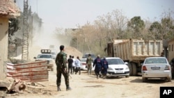 This photo released March, 22, 2108, by the Syrian official news agency SANA, shows Syrian government forces overseeing the evacuation by buses of rebel fighters and their families, at a checkpoint in eastern Ghouta, Syria.