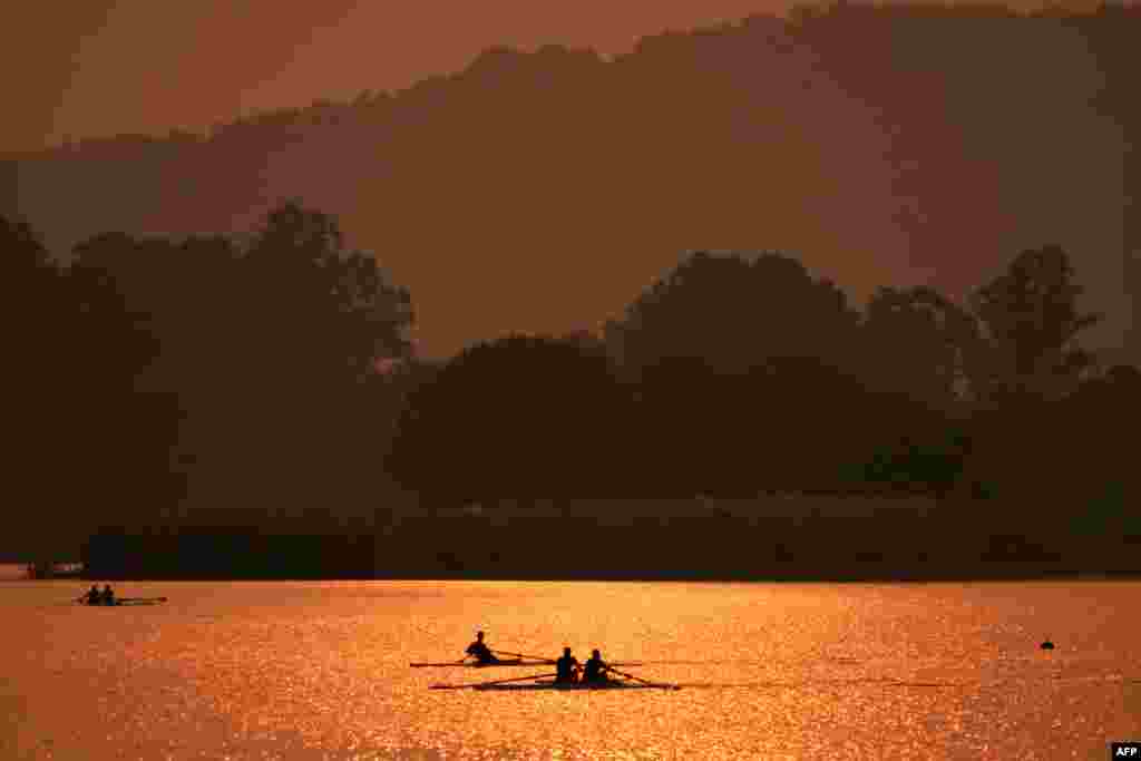 Row-men with their boats are silhouetted in the waters of Sukhna Lake during sunrise in Chandigarh, India.