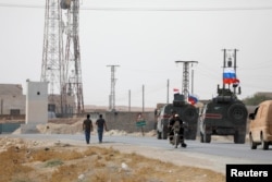 FILE - Russian and Syrian national flags flutter on military vehicles near Manbij, Syria, Oct. 15, 2019.