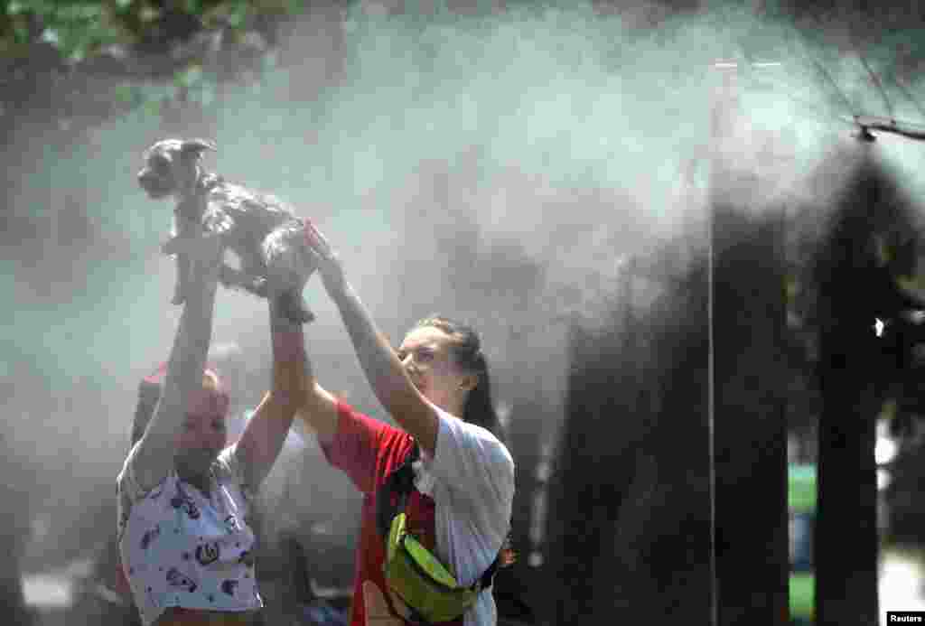 Girls refresh themselves and their dog with water spray frames set along the central street of the Ukrainian capital of Kyiv during a heatwave.