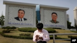 지난해 5월 북한 평양의 김일성, 김정일 초상화 앞에서 한 남성이 스마트폰을 사용하고 있다. (자료사진)