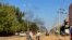 FILE — People displaced by the conflict in Sudan walk along road as smoke billows in the distance during clashes in Wad Madani, the capital of al-Jazirah state, on December 16, 2023.