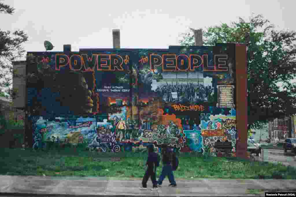 Des enfants du quartier marchent devant une autre fresque murale qui représente Freddie Gray avec le slogan &quot;le pouvoir du peuple&quot;. Baltimore, le 6 mai 2016. (VOA/ Nastasia Peteuil)