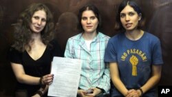 Pussy Riot members, from left, Maria Alekhina, Yekaterina Samutsevich, and Nadezhda Tolokonnikova show the court's verdict as they sit in a glass cage at a courtroom in Moscow, August 17, 2012.