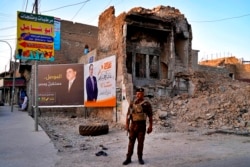 FILE - An Iraqi federal policeman stands guard near campaign posters for parliamentary elections that are displayed near destroyed buildings from fighting between Iraqi forces and the Islamic State group in Mosul, Iraq, Oct. 3, 2021.
