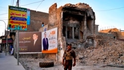 FILE - An Iraqi federal policeman stands guard near campaign posters for parliamentary elections that are displayed near destroyed buildings from fighting between Iraqi forces and the Islamic State group in Mosul, Iraq, Oct. 3, 2021.