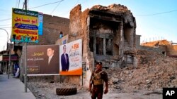 FILE - An Iraqi federal policeman stands guard near campaign posters for parliamentary elections that are displayed near destroyed buildings from fighting between Iraqi forces and the Islamic State group in Mosul, Iraq, Oct. 3, 2021.