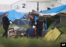 Greek policemen stand next to migrants at a makeshift refugee camp at the Greek-Macedonian border near the northern Greek village of Idomeni, May 24, 2016.